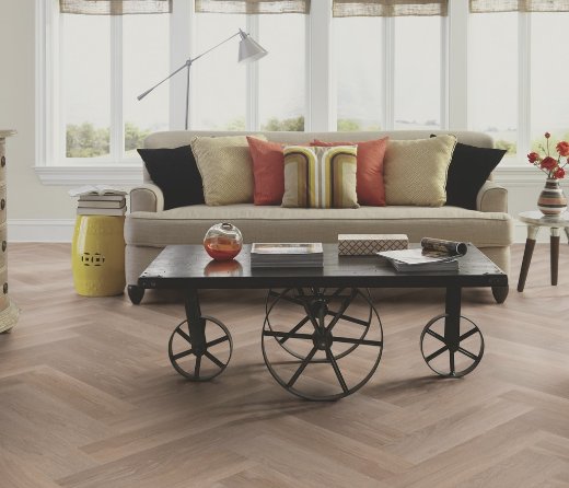 Visgraat PVC vloer in een woonkamer met een bank en tafel met wielen.