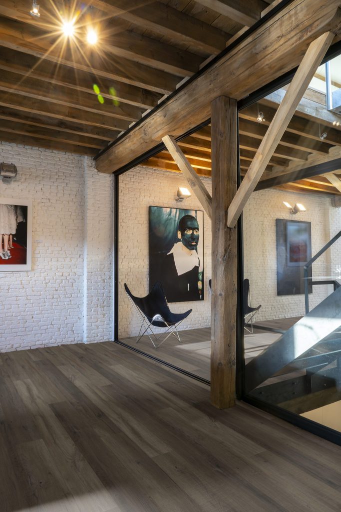 Kunstgalerij met houten balken, glazen wanden, moderne kunstwerken en donkere houtlook vloer in industriële stijl.