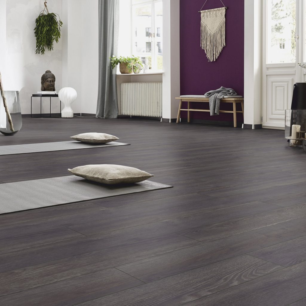 rustige yogastudio met donkere houtlook vloer, meditatiekussens, paarse accentmuur en sfeervolle minimalistische inrichting.
