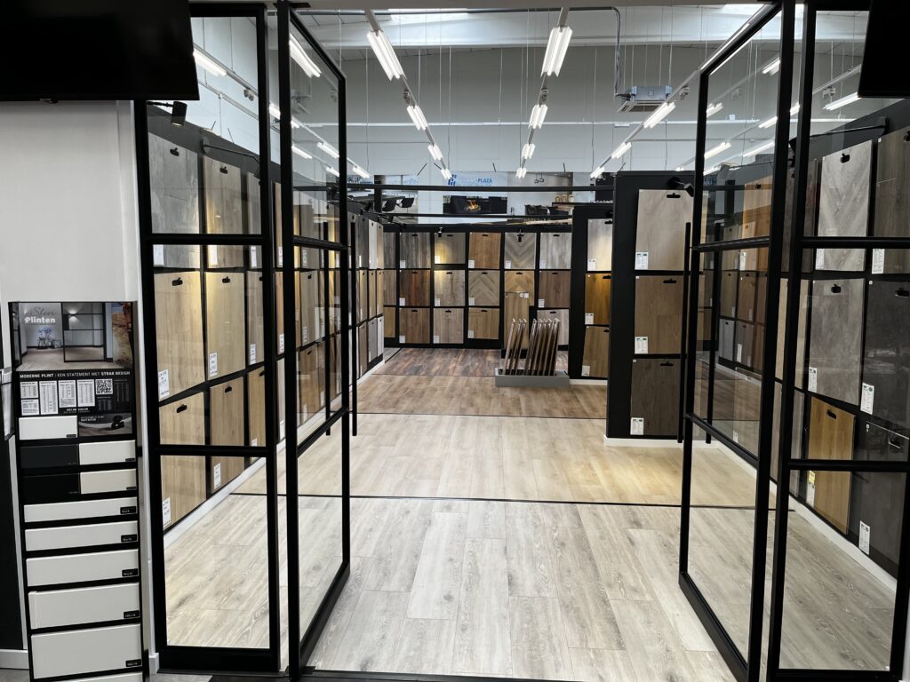 Showroom met diverse vloerpanelen in verschillende hout- en steendecors, overzichtelijk gepresenteerd aan zwarte wanden