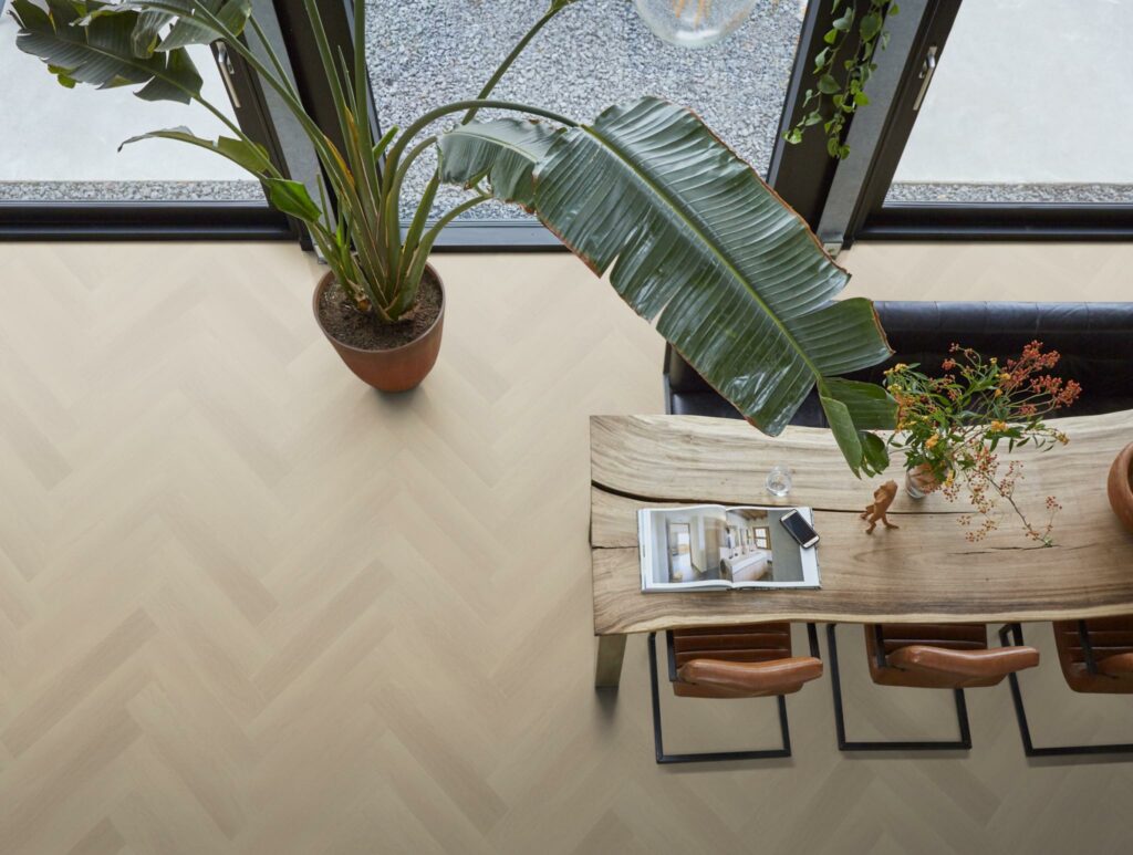 Birdview van een visgraat vloer in een eetkamer met grote plant en een houten tafel met industriële stoelen.