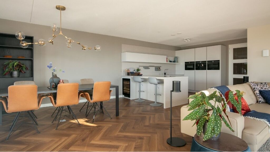 Donkere visgraatvloer in een open woonconcept met een woonkamer, eetkamer en keuken met bar.