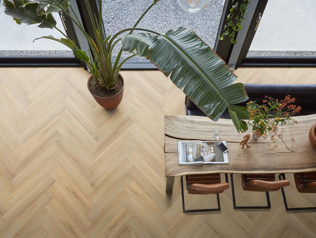 Bird’s-eye view van een visgraat vloer in een bedrijfspand met een grote plant en tafel met tijdschriften.